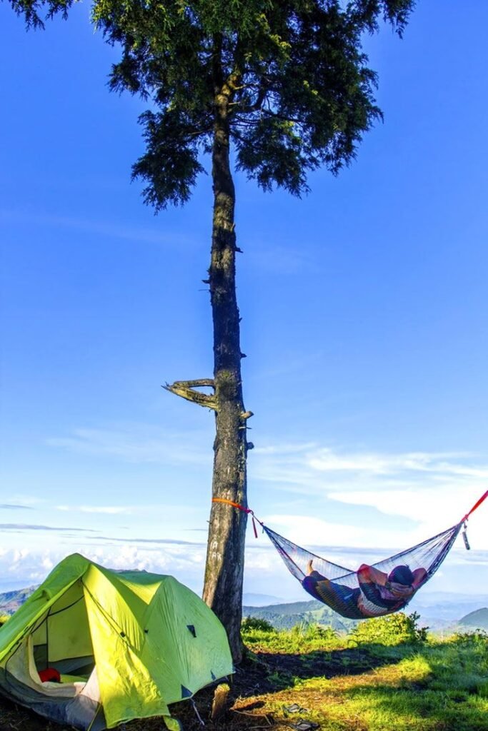 Relaxed Man Lying In A Hammock Beside The Camping Tent With Blue Sky 